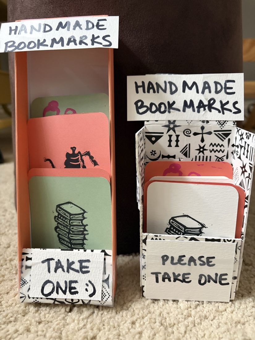 Two handmade dispenser boxes of little prints, labeled handmade bookmarks and please take one, stocked with small linocut cards